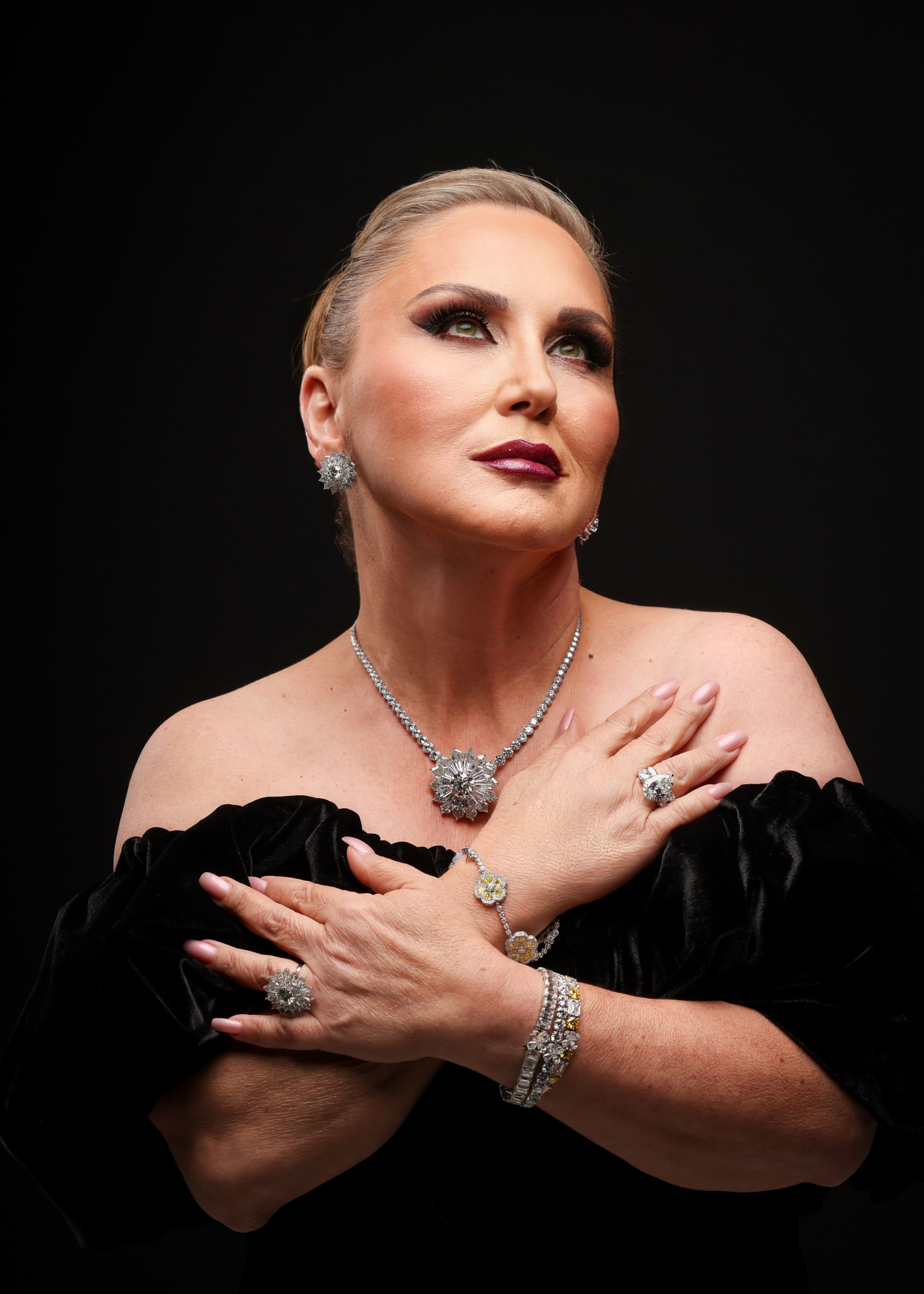 Elegant woman in black velvet with dazzling diamond jewelry poses against black background.