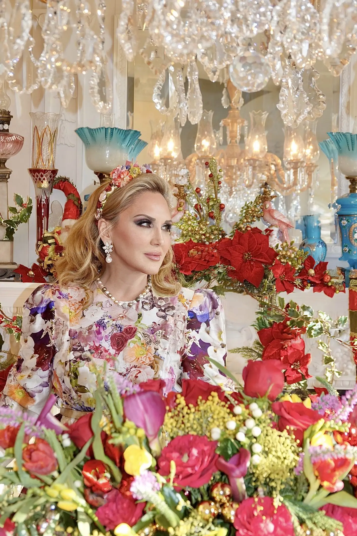 A woman adorned in floral attire surrounded by vibrant flowers and ornate decor.